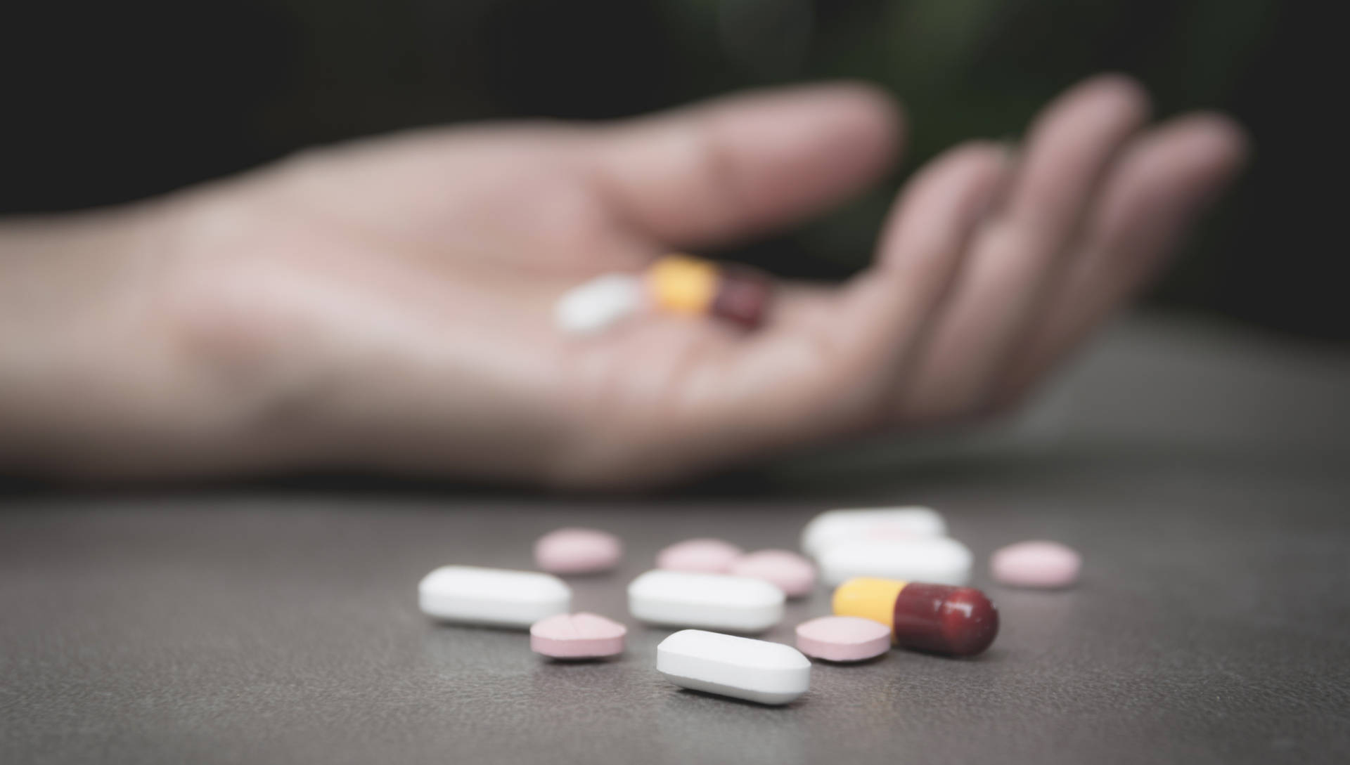 Open hand holding selection of pills with others spilled nerby