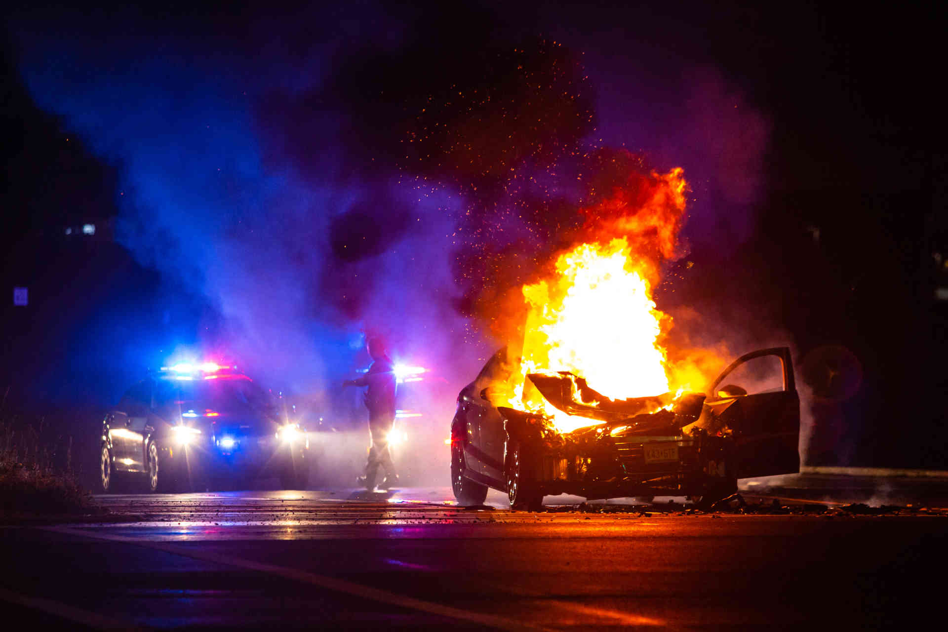 Car on fire at night, with a police car beside it